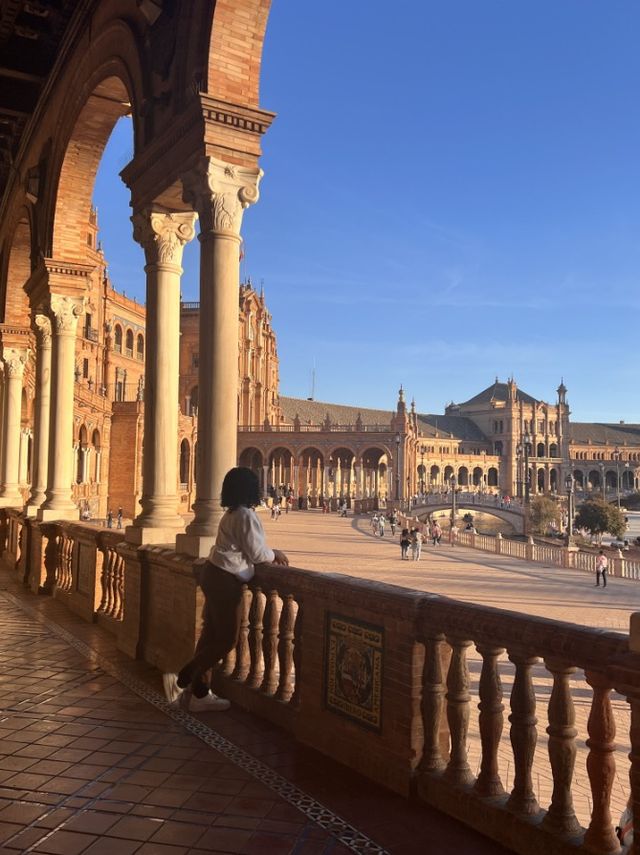 Faith leaning on a tiled balustrade at a grand plaza of arches at sunset