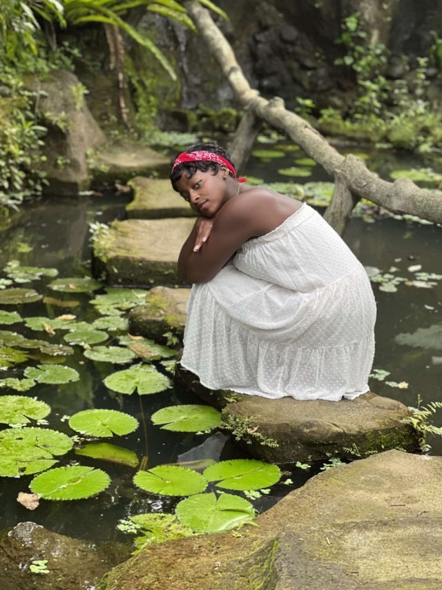 Faith in a white dress crouched on a stone in a lily pond